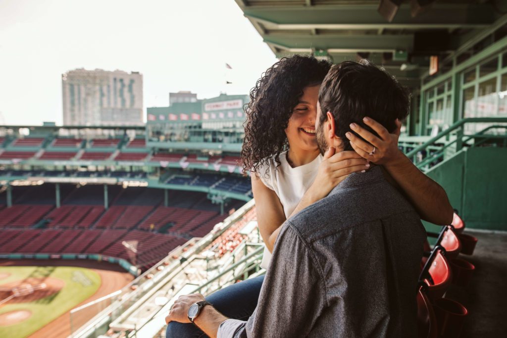 Couple poses in the bleachers at Fenway Park during their Boston engagement photo session